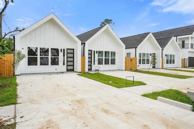 view of front facade featuring driveway, board and batten siding, and fence