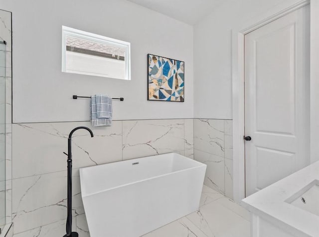 bathroom featuring a wainscoted wall, a sink, tile walls, marble finish floor, and a soaking tub