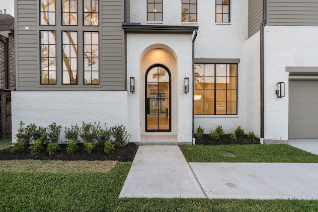 entrance to property featuring a garage, brick siding, and a yard