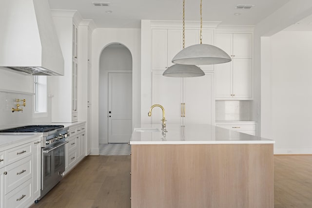 kitchen with visible vents, a sink, high end stainless steel range, wall chimney exhaust hood, and a kitchen island with sink