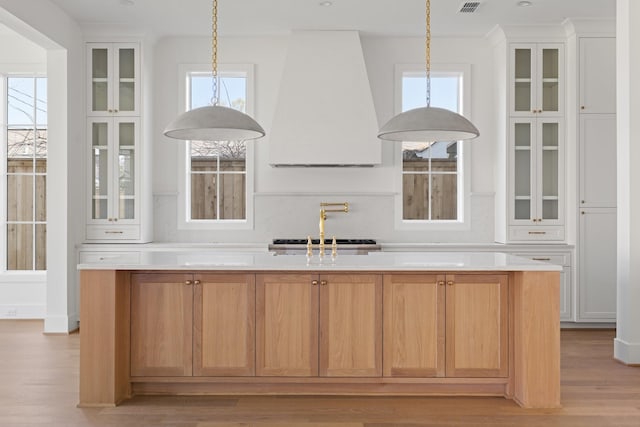 kitchen with light wood-style flooring, light countertops, custom range hood, white cabinetry, and decorative light fixtures