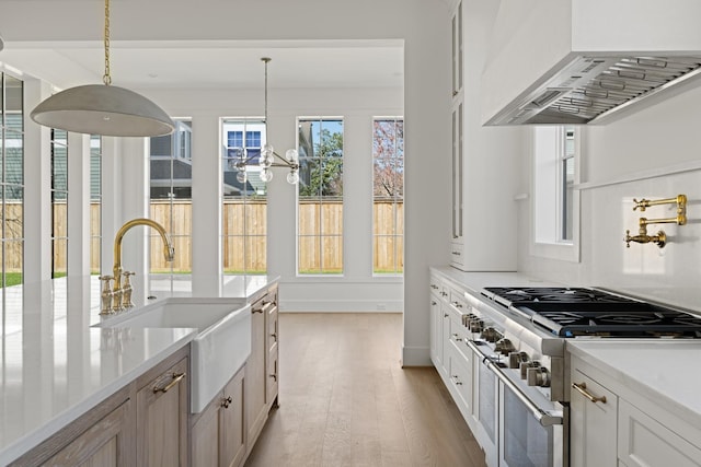 kitchen with light wood-type flooring, pendant lighting, a sink, double oven range, and wall chimney range hood