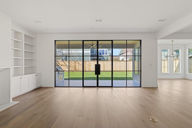 unfurnished room featuring built in features, wood finished floors, and a chandelier