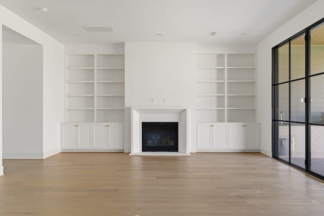 unfurnished living room with wood finished floors, a wealth of natural light, and a fireplace with raised hearth