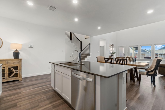 kitchen with dark countertops, dark wood-style flooring, stainless steel dishwasher, white cabinetry, and a sink