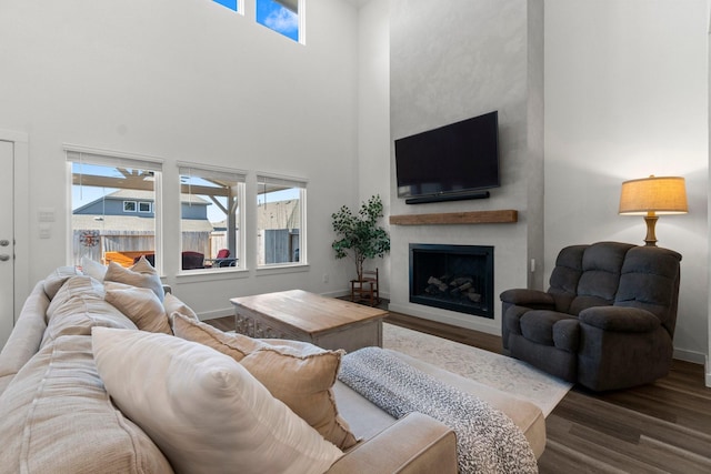 living room with a towering ceiling, a fireplace, baseboards, and wood finished floors