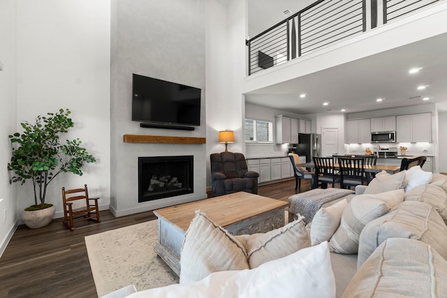 living room featuring a fireplace, recessed lighting, a high ceiling, dark wood-type flooring, and baseboards