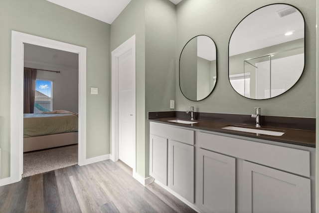 ensuite bathroom with double vanity, baseboards, a sink, and wood finished floors