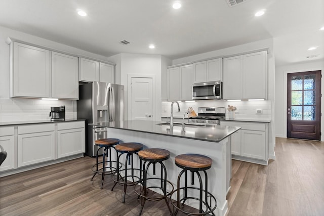 kitchen featuring visible vents, appliances with stainless steel finishes, a breakfast bar, wood finished floors, and a sink