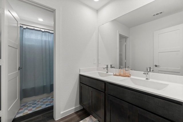 full bathroom with double vanity, visible vents, a sink, and wood finished floors