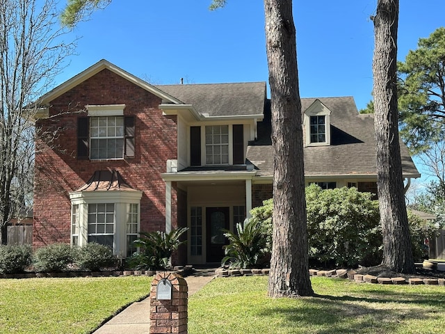 view of front of home featuring roof with shingles, a front lawn, and brick siding