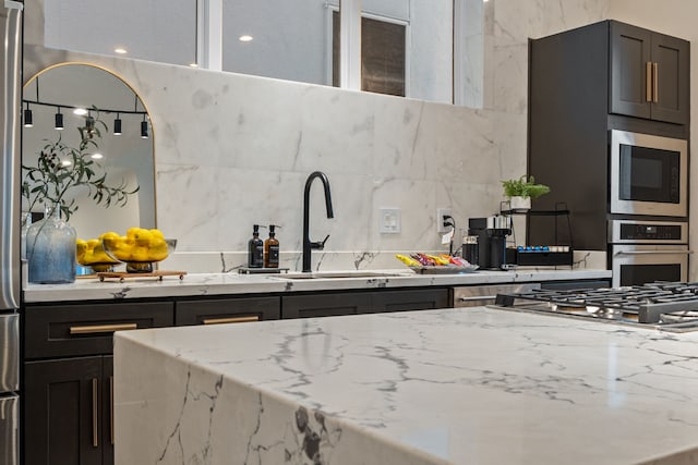 kitchen with appliances with stainless steel finishes, backsplash, a sink, and light stone counters