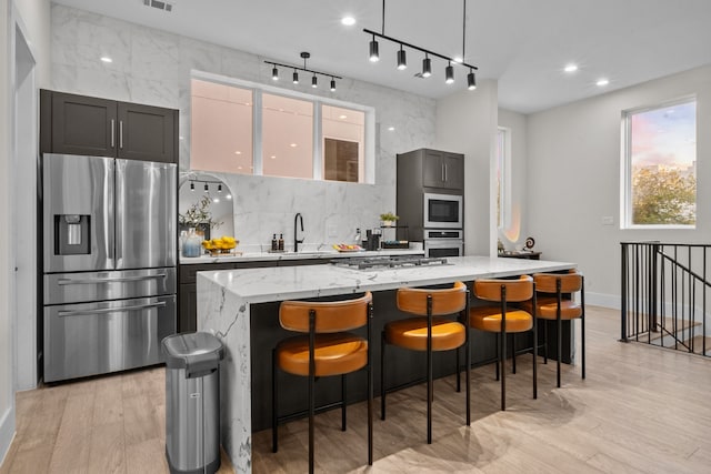 kitchen featuring a kitchen island, appliances with stainless steel finishes, a kitchen breakfast bar, light stone countertops, and backsplash