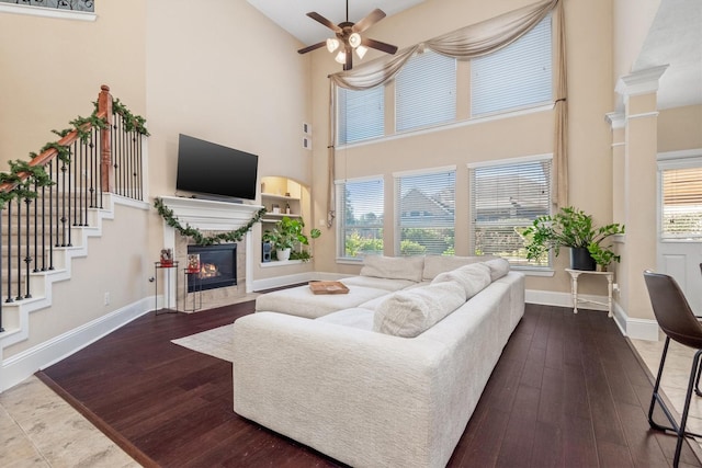 living room featuring a fireplace, a towering ceiling, hardwood / wood-style flooring, and baseboards