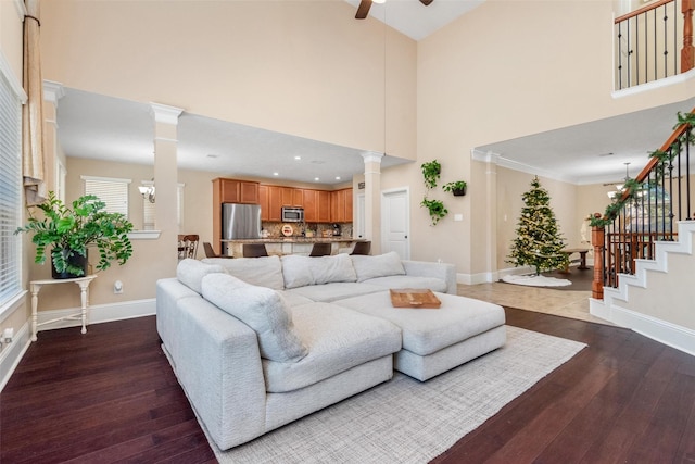 living area featuring baseboards, hardwood / wood-style floors, stairs, and ornate columns