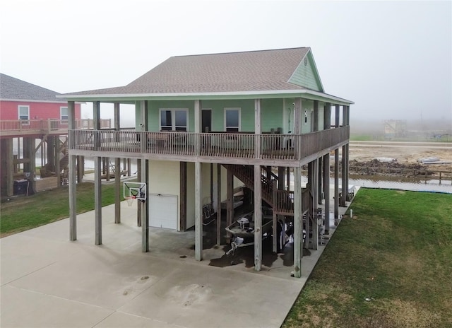 back of property featuring a garage, covered porch, a shingled roof, a water view, and a yard