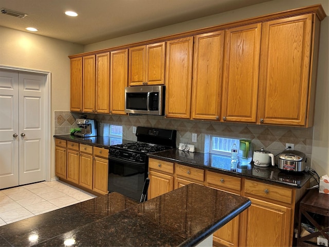 kitchen with stainless steel microwave, backsplash, black range with gas cooktop, and brown cabinetry