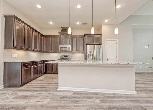 kitchen with stainless steel appliances, dark brown cabinets, an island with sink, and light wood-style flooring