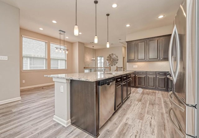 kitchen featuring appliances with stainless steel finishes, dark brown cabinetry, a sink, and a center island with sink