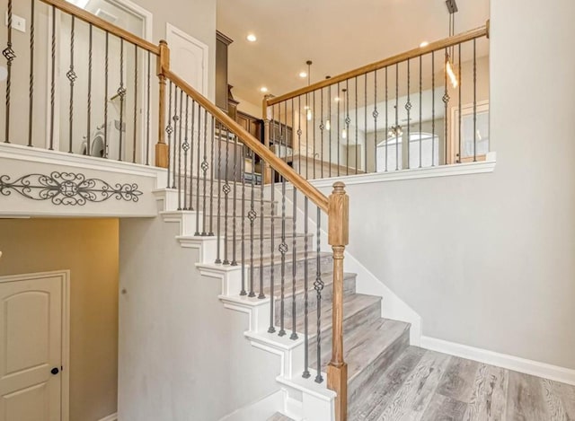 stairs with baseboards, wood finished floors, and recessed lighting