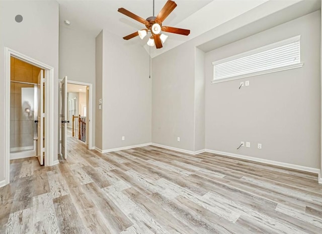 spare room featuring a towering ceiling, light wood-style flooring, baseboards, and a ceiling fan