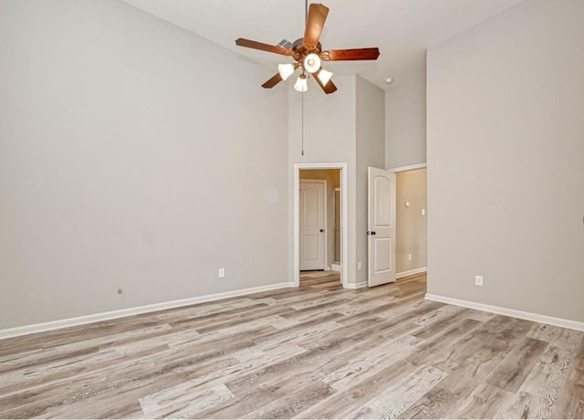 empty room with baseboards, ceiling fan, high vaulted ceiling, and light wood-style floors