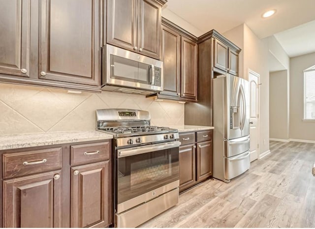 kitchen with baseboards, light wood-style floors, appliances with stainless steel finishes, decorative backsplash, and light stone countertops