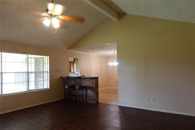 unfurnished room with ceiling fan with notable chandelier, lofted ceiling with beams, a textured ceiling, wood finished floors, and baseboards