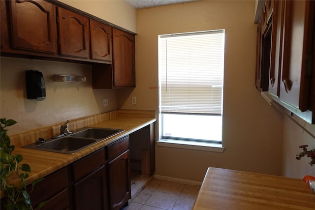 kitchen with light tile patterned flooring, light countertops, baseboards, and a sink