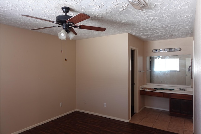 unfurnished bedroom featuring a textured ceiling, wood finished floors, baseboards, and a sink