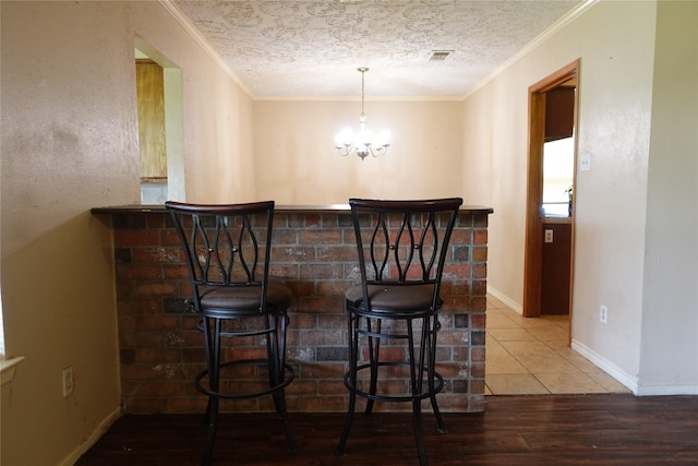 bar with a textured ceiling, baseboards, a chandelier, wood finished floors, and crown molding