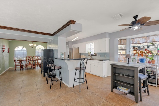 kitchen with dark countertops, visible vents, a kitchen breakfast bar, stainless steel refrigerator with ice dispenser, and white cabinetry