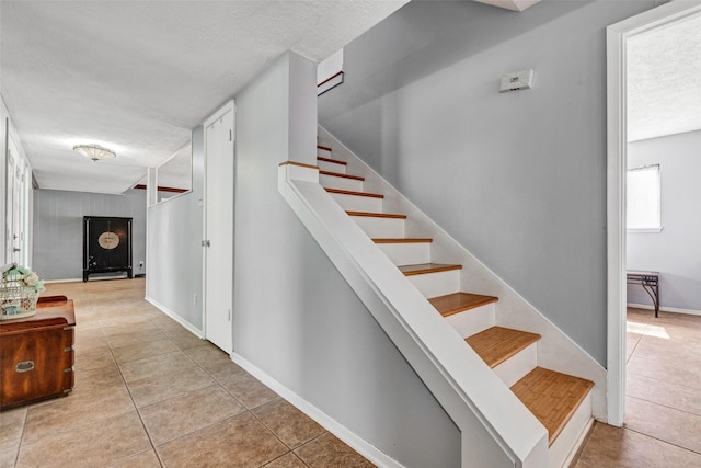 staircase featuring baseboards, a textured ceiling, and tile patterned flooring