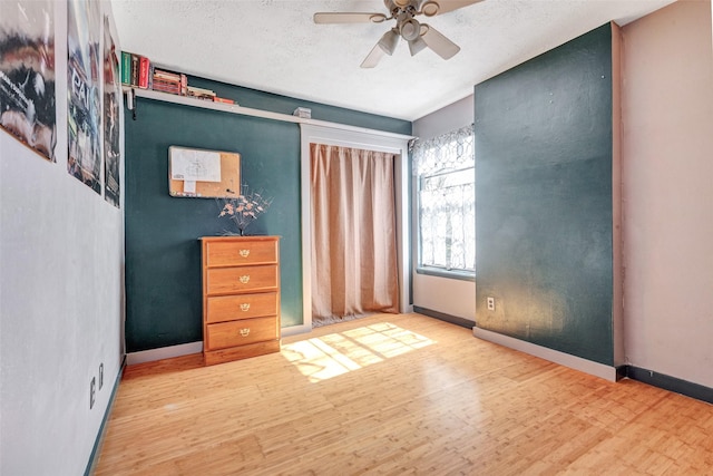 unfurnished bedroom featuring baseboards, a textured ceiling, wood finished floors, and a ceiling fan