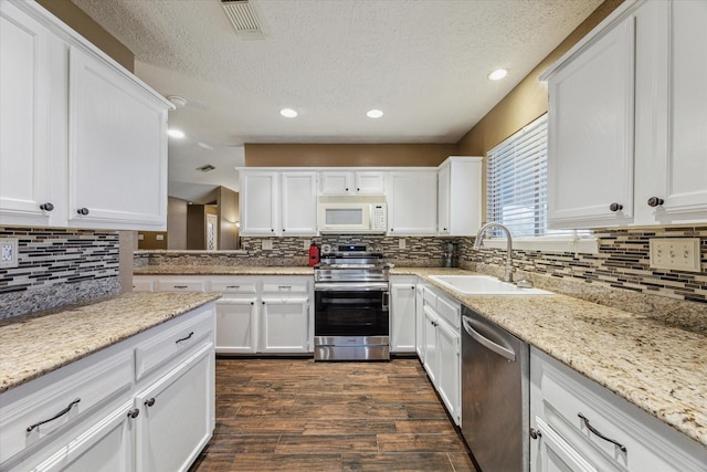 kitchen with appliances with stainless steel finishes, dark wood-type flooring, a sink, and white cabinetry