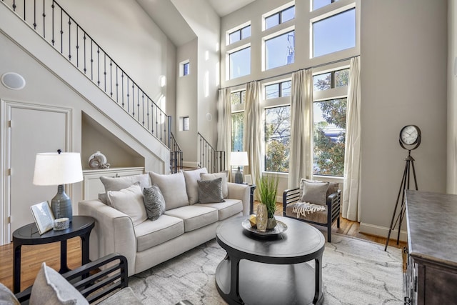 living room featuring baseboards, light wood-type flooring, stairs, and a high ceiling