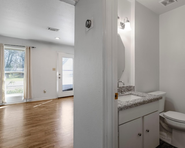 bathroom featuring toilet, vanity, wood finished floors, and visible vents