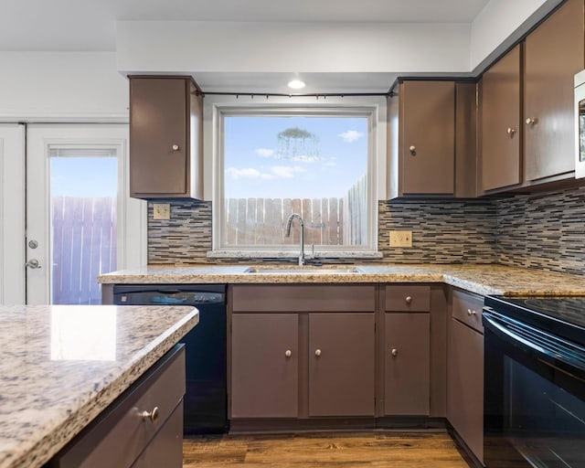 kitchen featuring wood finished floors, backsplash, a sink, light stone countertops, and black appliances