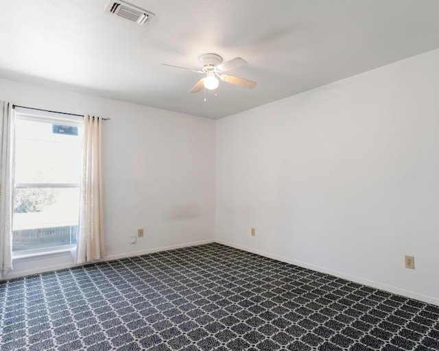 spare room with ceiling fan, dark colored carpet, visible vents, and baseboards