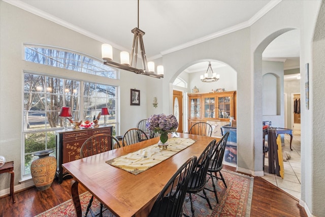 dining area with arched walkways, crown molding, wood finished floors, a chandelier, and baseboards