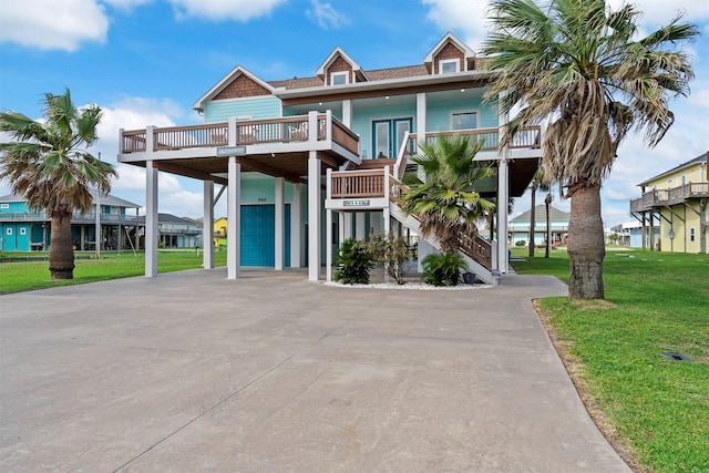 coastal inspired home featuring a carport, concrete driveway, a front lawn, and stairs