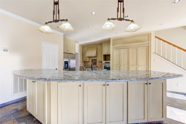 kitchen with cream cabinets, stone finish floor, baseboards, appliances with stainless steel finishes, and premium range hood