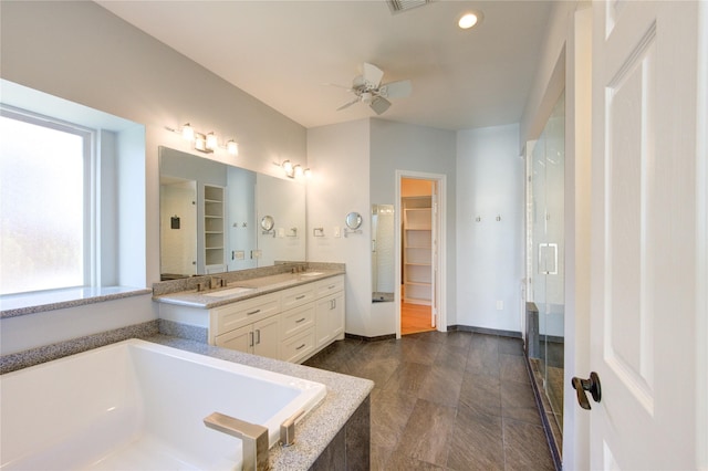 bathroom featuring a ceiling fan, a bath, a sink, double vanity, and a walk in closet