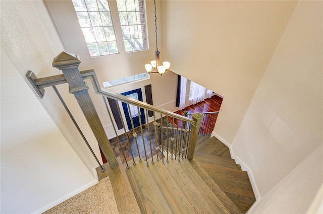 stairway featuring an inviting chandelier, baseboards, and a high ceiling