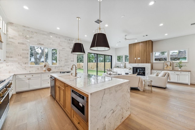 kitchen with light wood finished floors, visible vents, light stone counters, a fireplace, and a sink