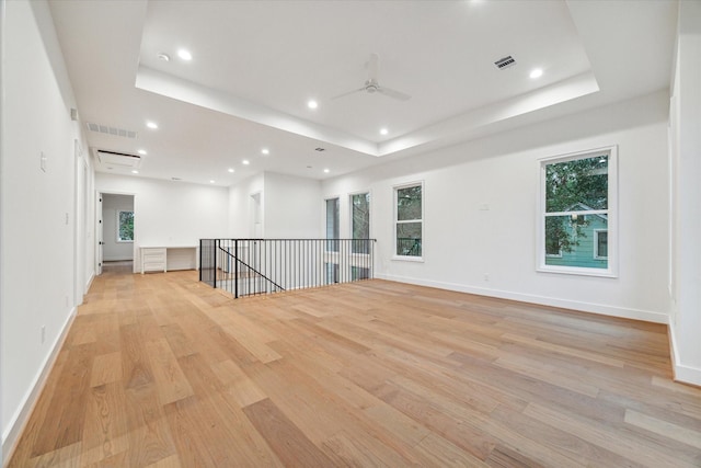 empty room with light wood-style floors, a raised ceiling, and visible vents