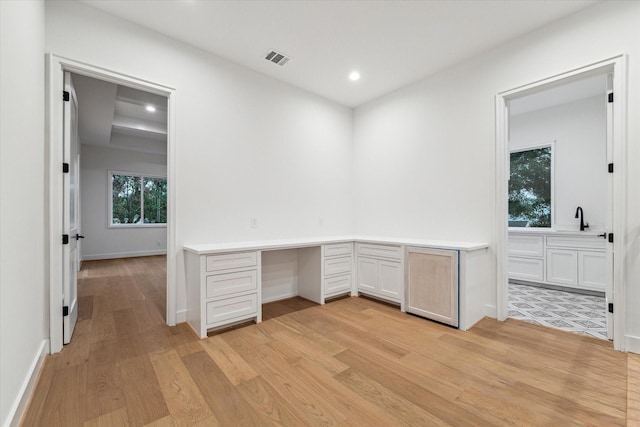 unfurnished office featuring recessed lighting, visible vents, light wood-style floors, built in study area, and a sink