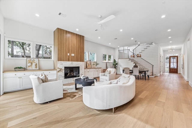 living room with visible vents, light wood-style flooring, stairway, a wealth of natural light, and a high end fireplace