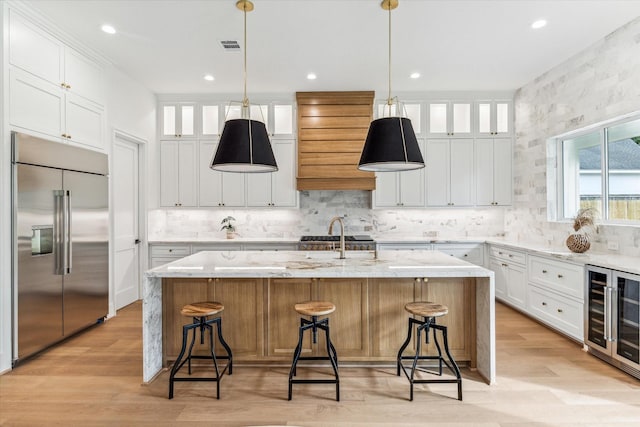 kitchen with wine cooler, built in refrigerator, a center island with sink, and white cabinets