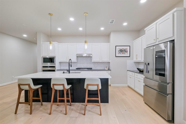 kitchen with under cabinet range hood, stainless steel appliances, a sink, visible vents, and decorative backsplash